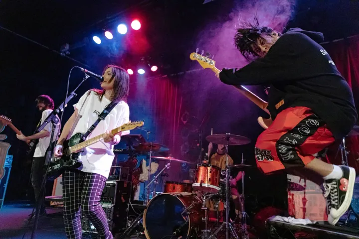 Stand Atlantic on stage under red and blue lights, Bonnie Fraser singing with a guitar while the bassist leaps in the air, 2019